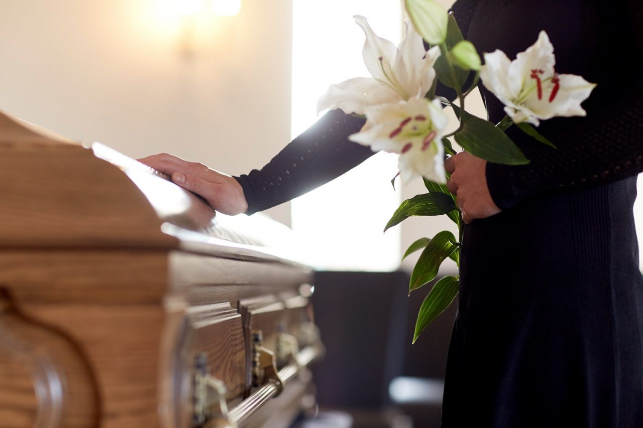 Mourner with lilies placing their hand on a funeral casket