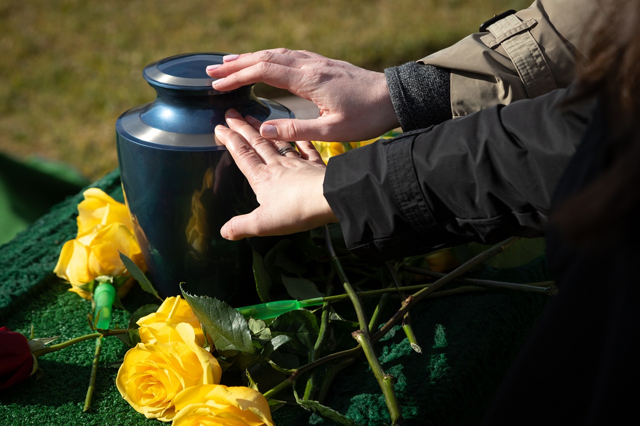 Hands touching a burial urn at an outdoor funeral